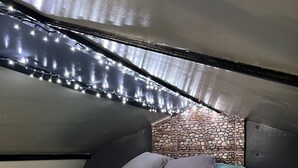 Ein Bett mit grüner Decke, zwei Kissen und einer Steinwand im Hintergrund.