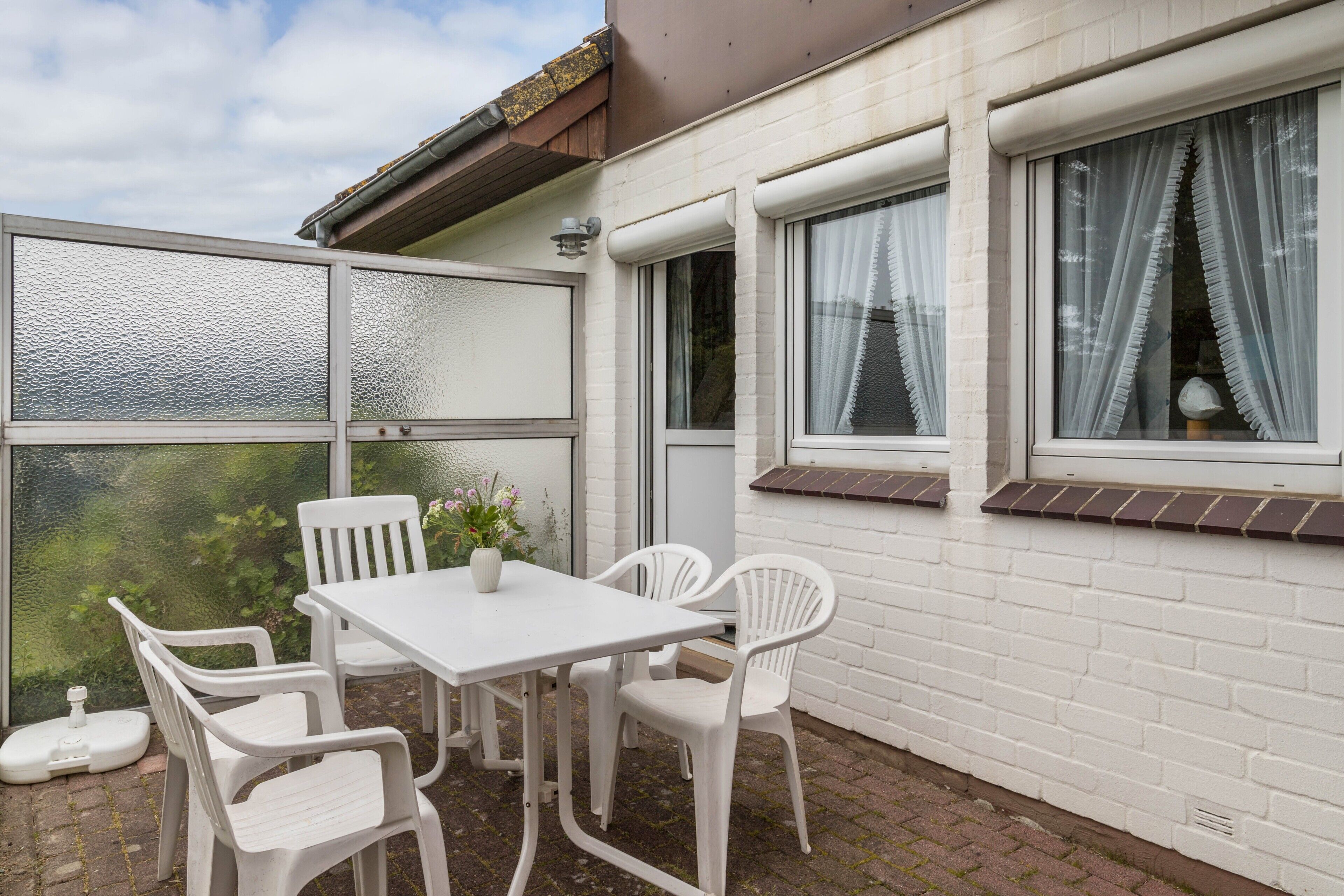 Een terras met een tafel en stoelen, een potplant en uitzicht door een raam.