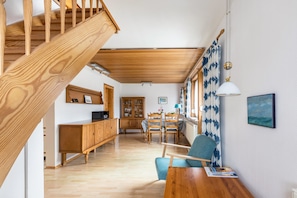 Un espacio habitable amplio con una escalera de madera, una mesa de comedor con sillas, un mueble de madera y vistas a través de ventanas grandes.