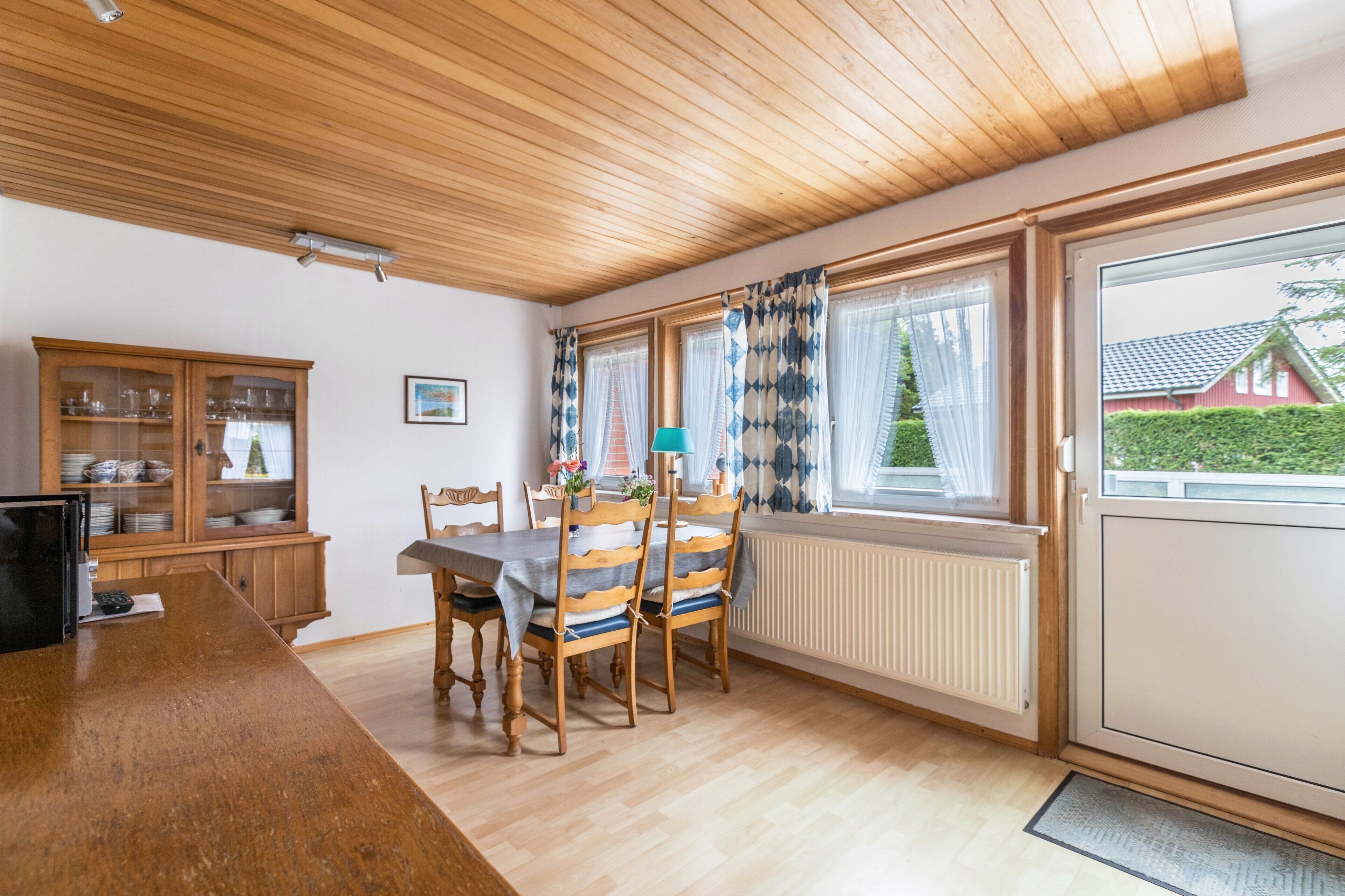 A dining area with a wooden table and chairs, a cabinet with glass doors, and a window with curtains.
