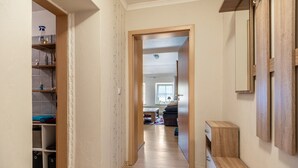Un corridoio con pavimento in legno, un armadio con ripiani, uno specchio e una porta che dà su un'altra stanza.