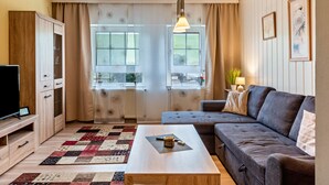 Un salon avec un canapé, une table basse, un téléviseur et une fenêtre avec des rideaux.