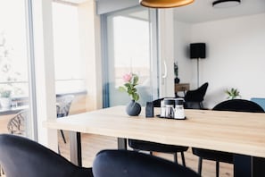 A modern dining area with a wooden table, black chairs, a vase with a flower, and a coffee maker.