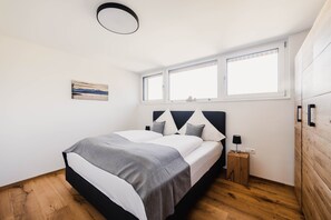 Une chambre à coucher comprenant un lit, une table de chevet, une lampe fixée au mur et une fenêtre avec des stores.