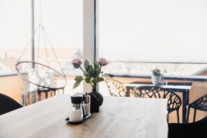 Una mesa de madera con un florero de flores rosas y saleros y pimenteros, una silla colgante y vistas a la playa.