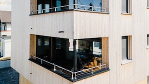 Un immeuble moderne à plusieurs étages, doté d’une façade en bois, de grandes fenêtres et d’un balcon.
