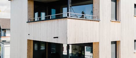 A modern multi-story building with a wooden facade, large windows, and a balcony.