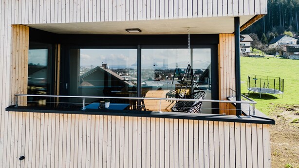 Ein modernes Gebäude mit Holzfassade, großen Fenstern und einem Balkon mit einer Hängematte.