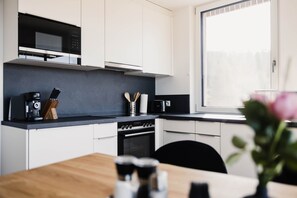 A modern kitchen with white cabinets, a black countertop, a microwave, and an oven.