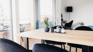 Ein zeitgemäßer Essbereich mit Holztisch, schwarzen Stühlen, einer Vase mit einer Blume und einer Kaffeemaschine.