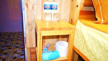 Un tavolo in legno con bottiglie d'acqua, bicchieri e un dispositivo blu in una stanza con un letto e un pavimento decorato.