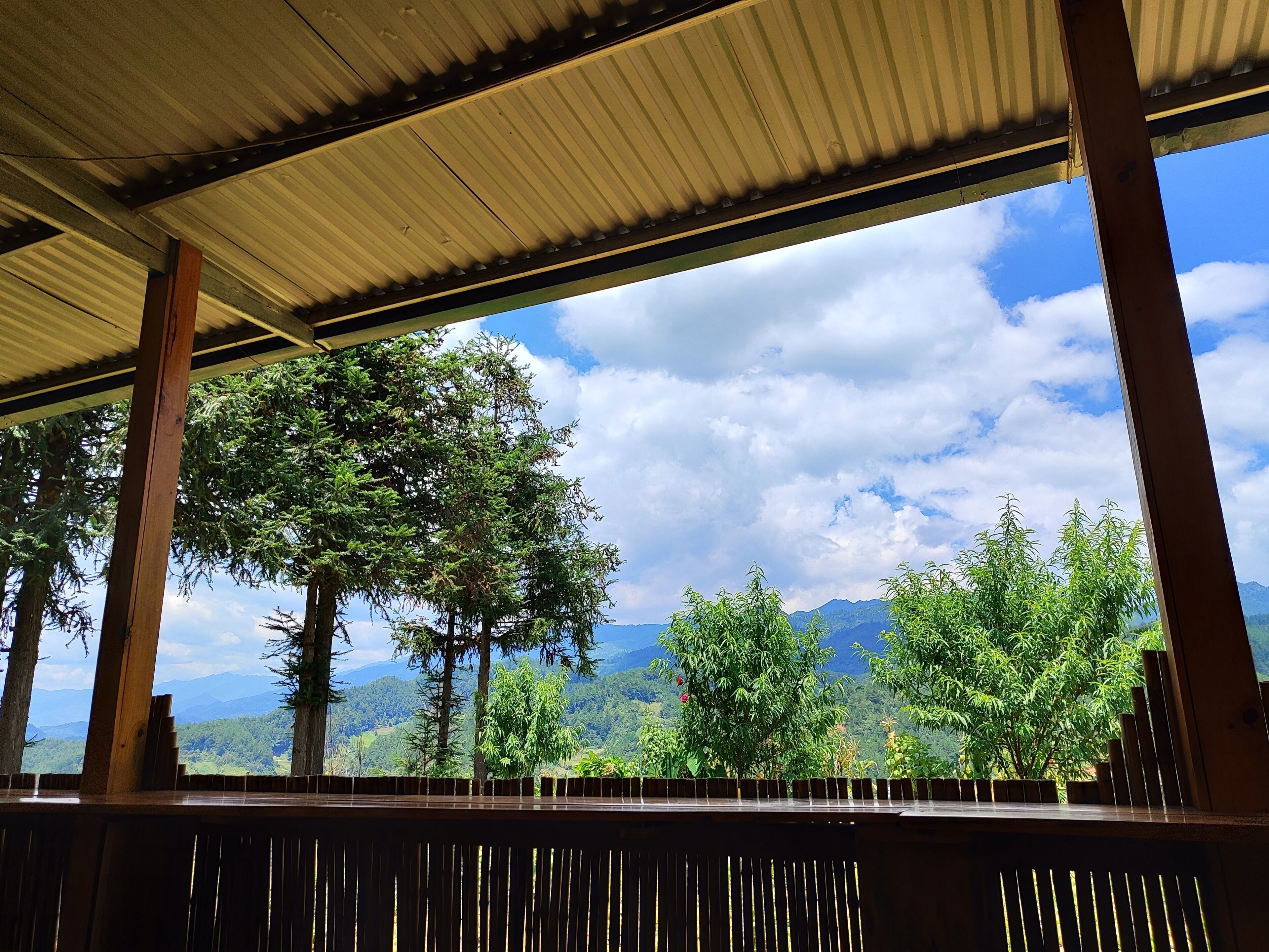 A covered outdoor area with a view of a mountainous landscape and trees.