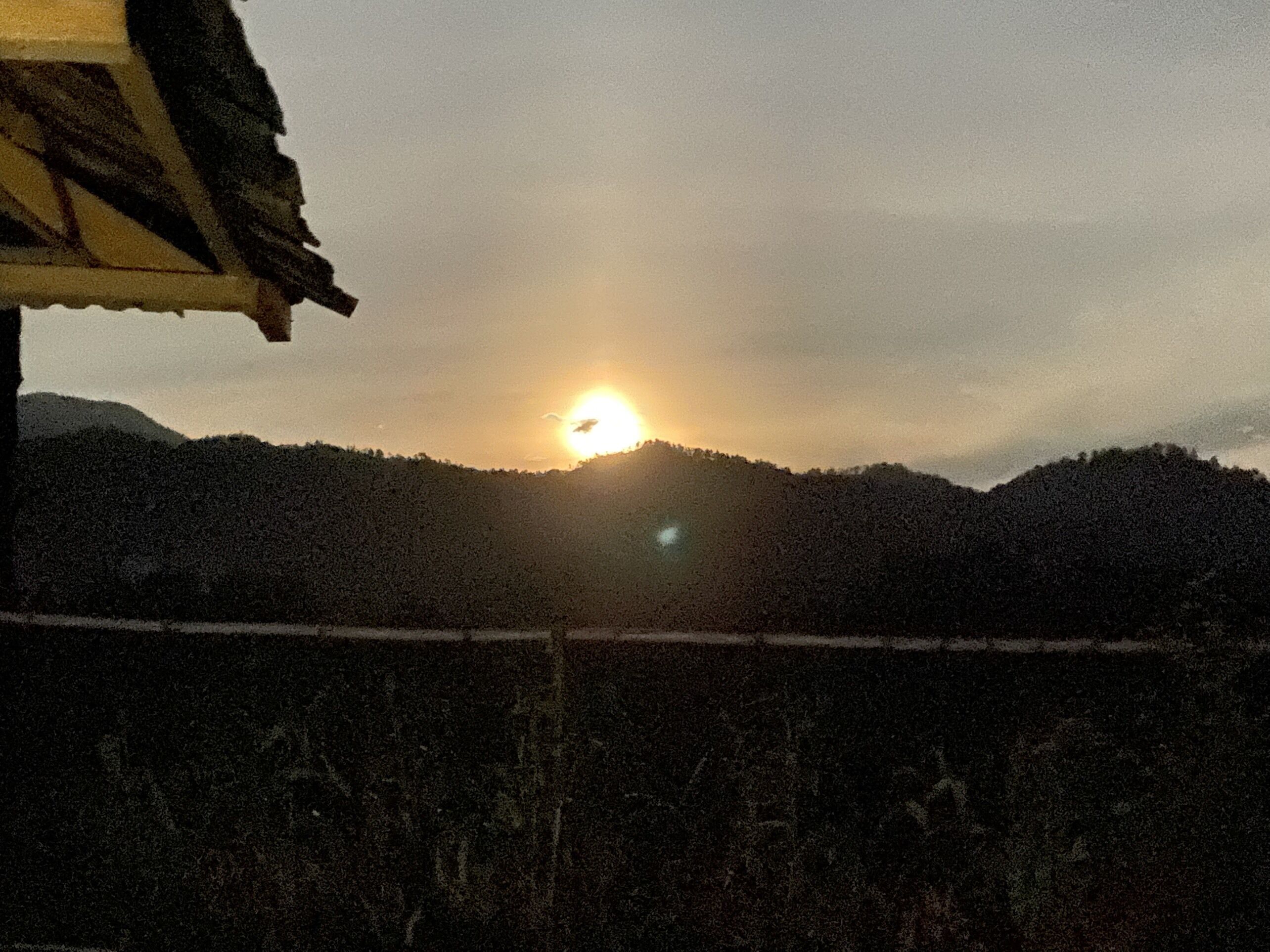 Un coucher de soleil sur un paysage montagneux, avec une maison au premier plan.