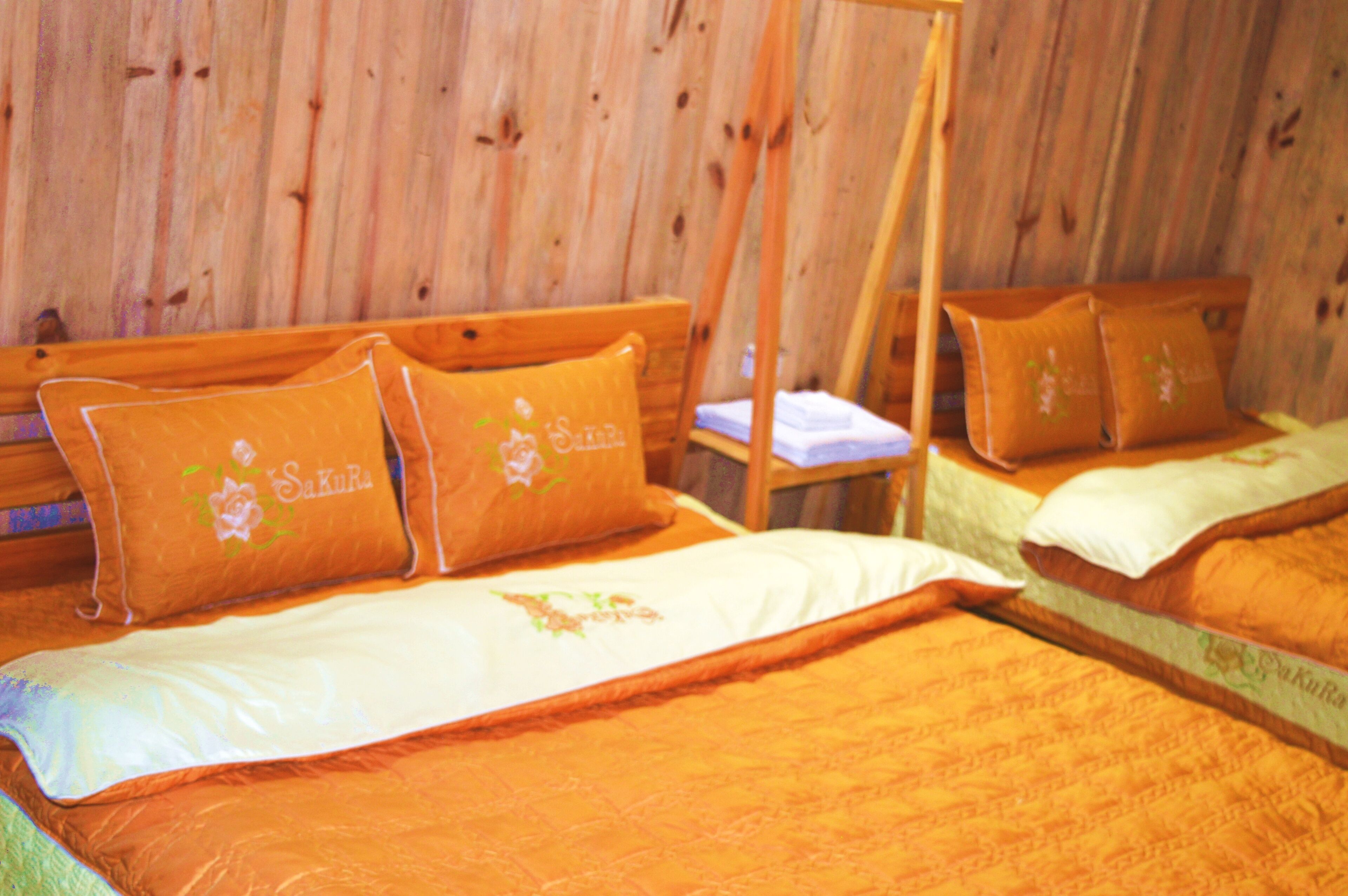 Una habitación con paredes de madera, dos camas con ropa de cama naranja y una cama con dosel de madera.