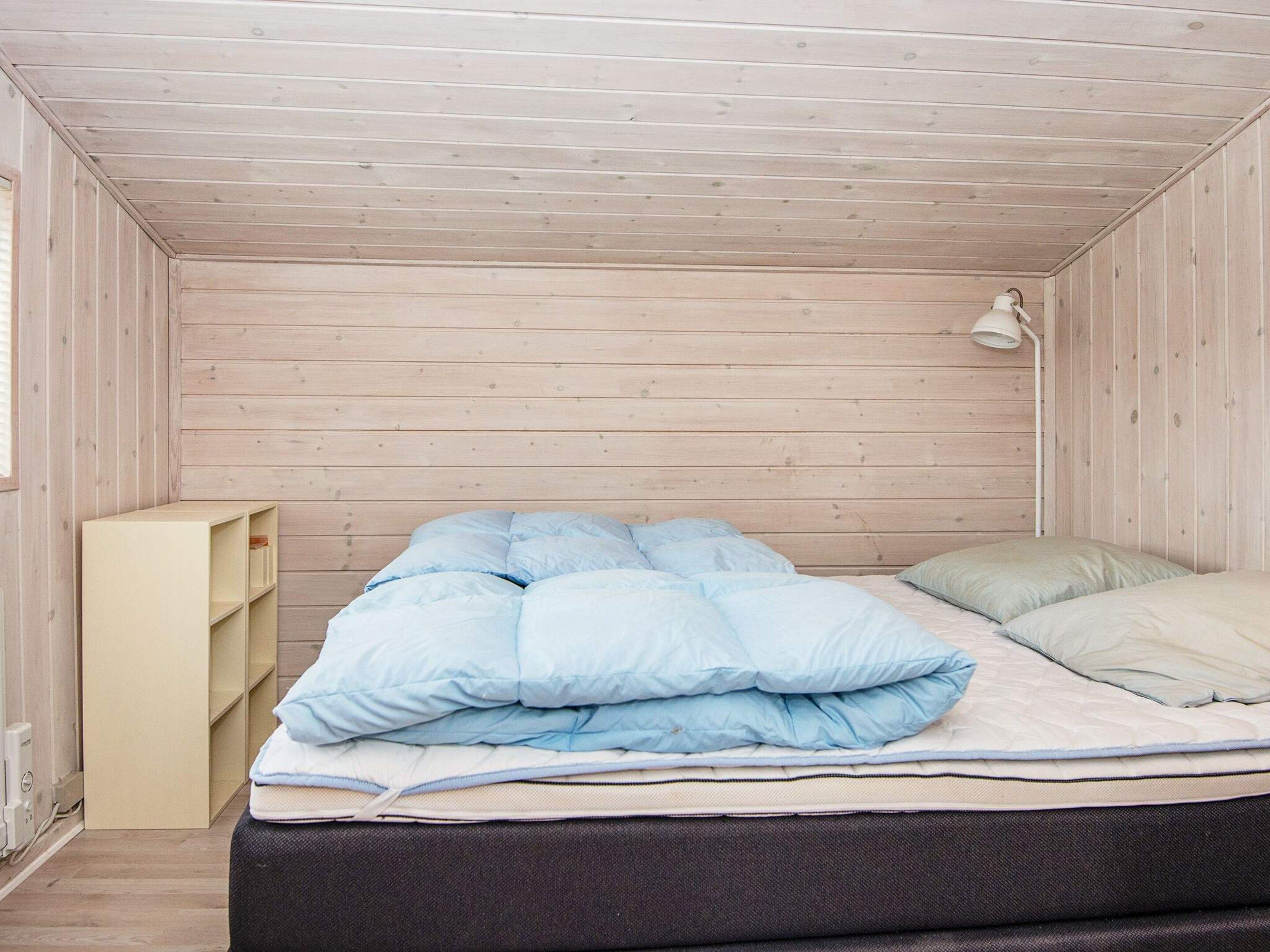 A bedroom with a bed, a bedside lamp, and a built-in shelf unit.