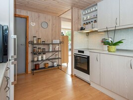 Una cocina con armarios de madera, horno empotrado y estante con frascos y utensilios de cocina.