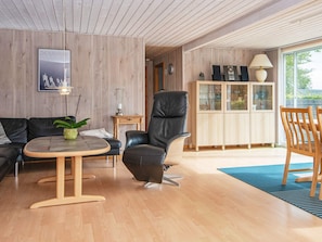 Una sala de estar moderna con un sofá de cuero, un sillón de cuero negro, una mesa de centro de madera y un aparador con puertas de vidrio.