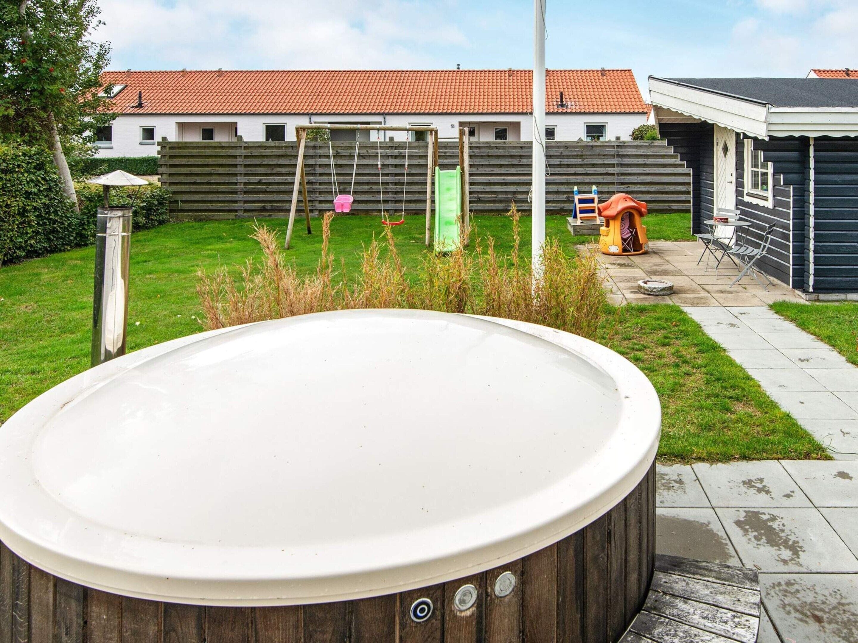 Jacuzzi al pati d'una casa amb terrassa de fusta, balancà i zona de jocs.