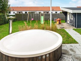 Un jacuzzi en un patio trasero con terraza de madera, un columpio y una zona de juegos.