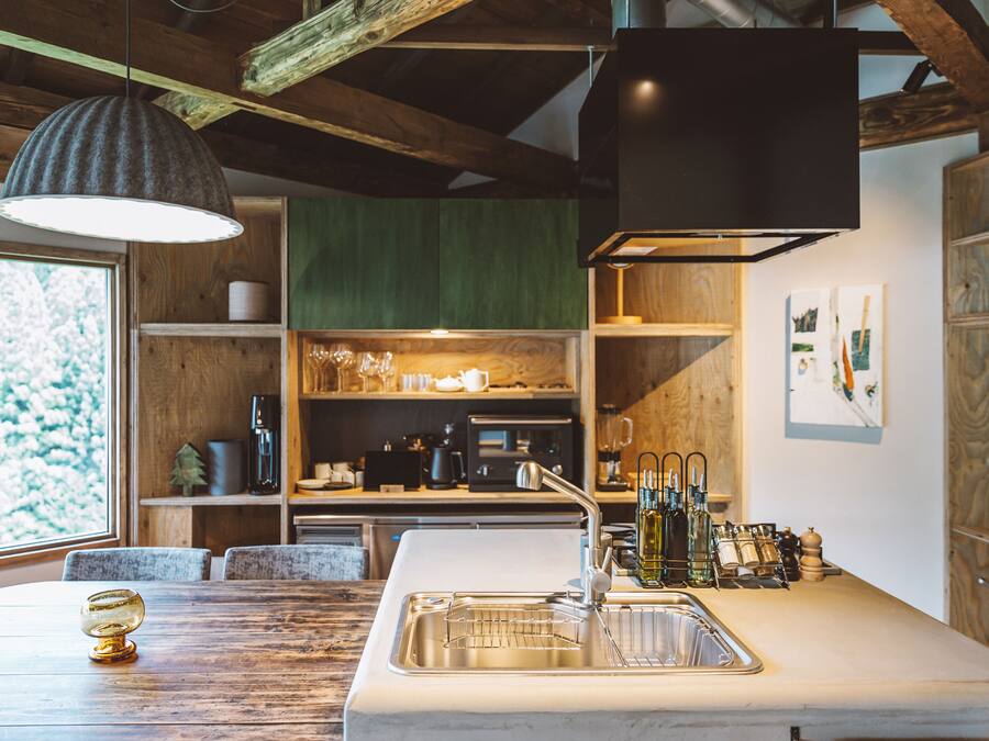 A modern kitchen with a large island, wooden beams, and a view of a snowy landscape.