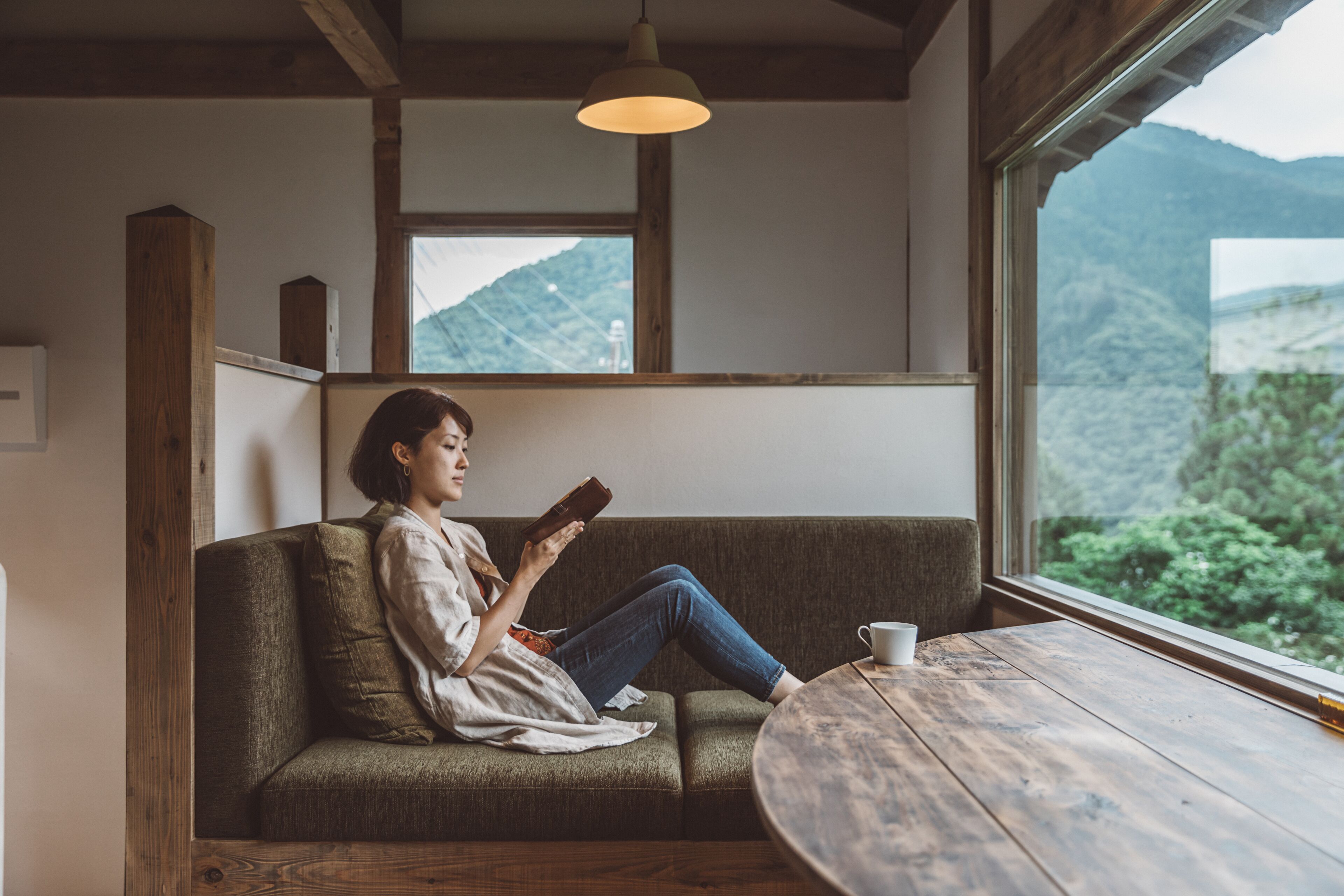 A person sitting on a sofa by a window with a view of mountains.