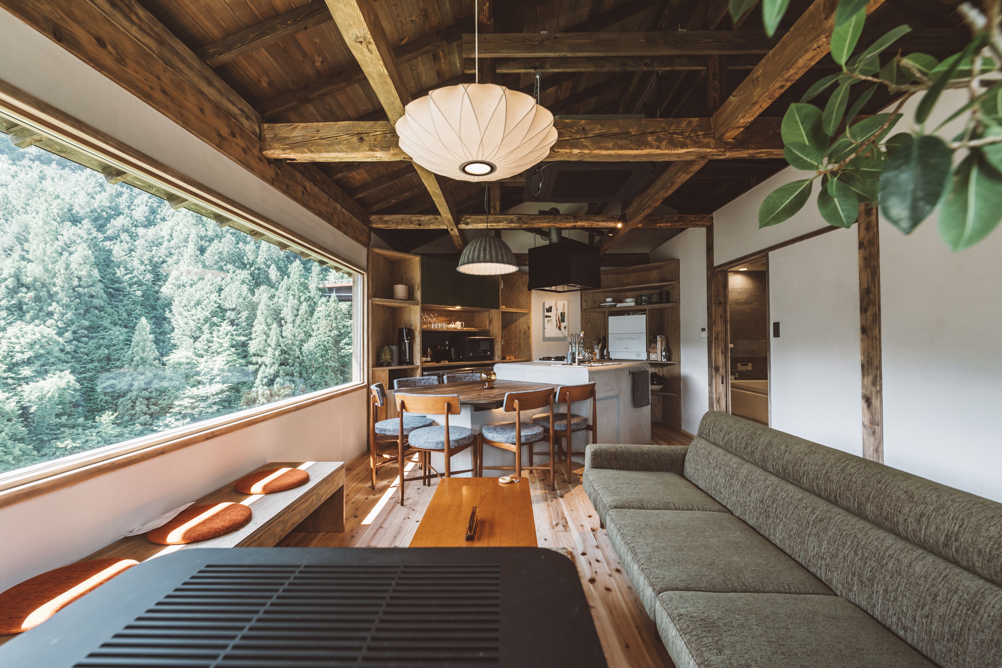Interior acogedor de una cabaña con zona de comedor de madera, un sofá y un ventanal con vistas a un bosque.