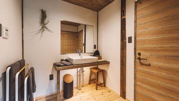 A modern bathroom with a wooden floor, a large mirror, a sink, and a wooden door.
