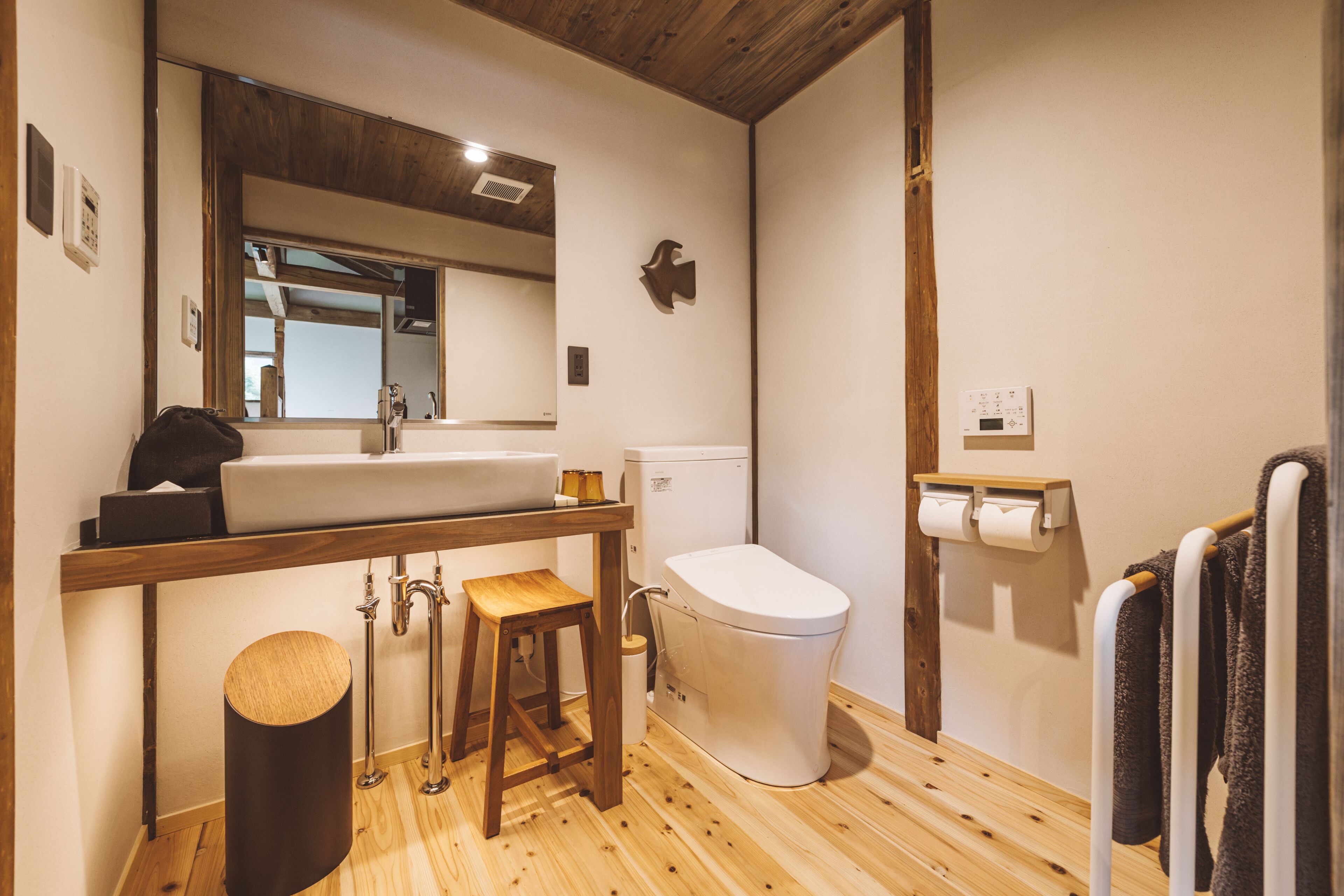 Un baño moderno con piso de madera, un lavamanos blanco, un inodoro y un espejo sobre el lavamanos.