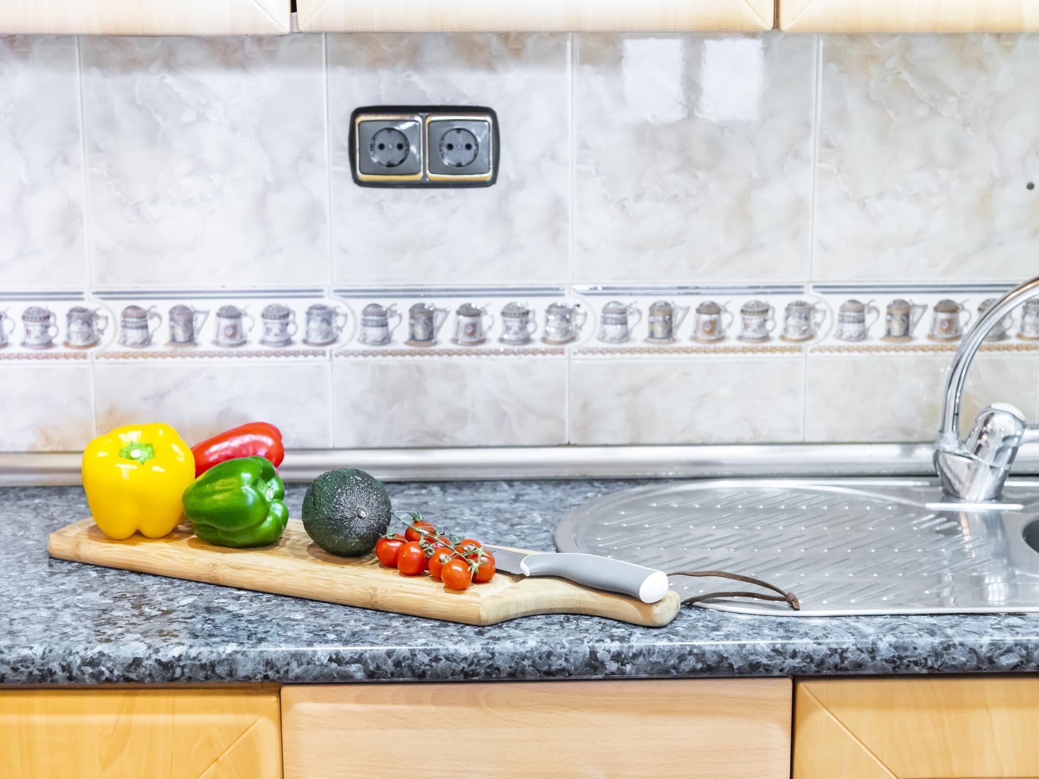 A kitchen with a granite countertop, a cutting board with vegetables, a knife, and a sink with a faucet.