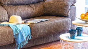 A brown sofa with a hat, sunglasses, and magazines on it. There is a small round table with two mugs and a bowl of fruit. - 9 Amarilla Bay Holiday Pool Terrace (Costa del Silencio)
