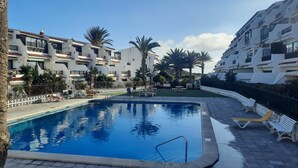 A swimming pool surrounded by a white building with balconies, palm trees, and a clear sky. - 9 Amarilla Bay Holiday Pool Terrace (Costa del Silencio)
