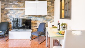 A modern living room with a stone wall, a flat-screen TV, two chairs, a dining table with a bottle of wine, and a window. - 9 Amarilla Bay Holiday Pool Terrace (Costa del Silencio)