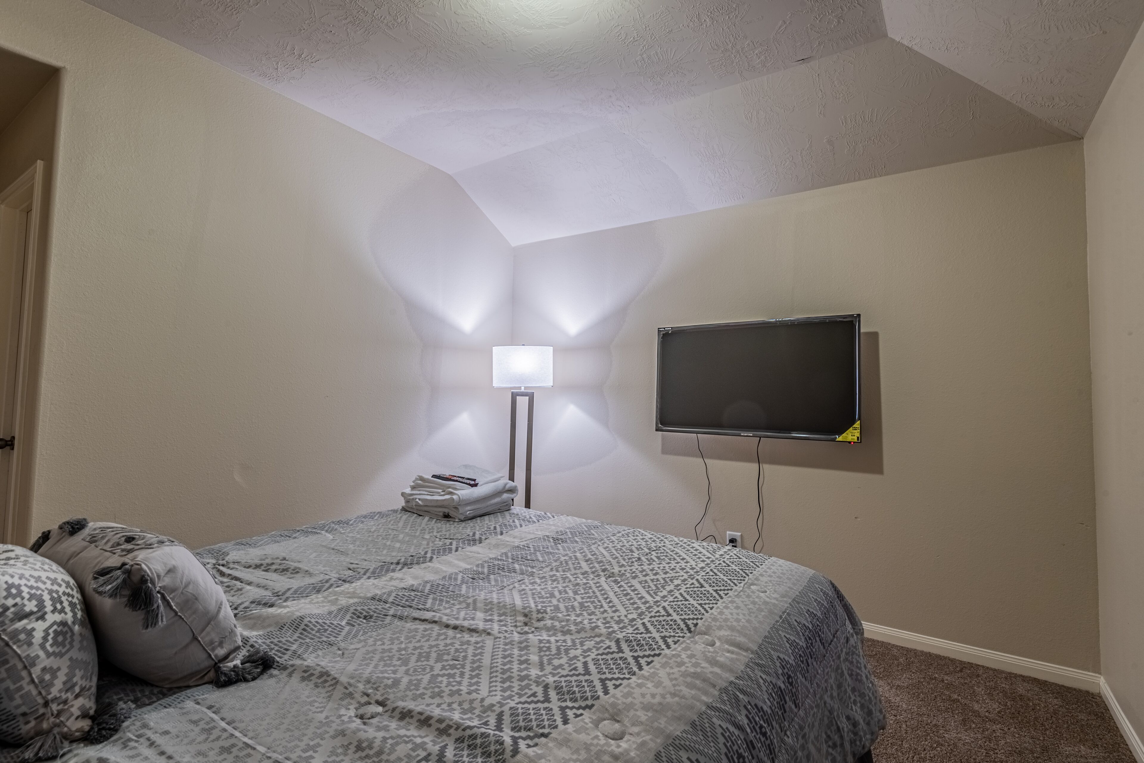 Une chambre à coucher comprenant un lit, un téléviseur à écran plat fixé au mur, une lampe de chevet et une porte.