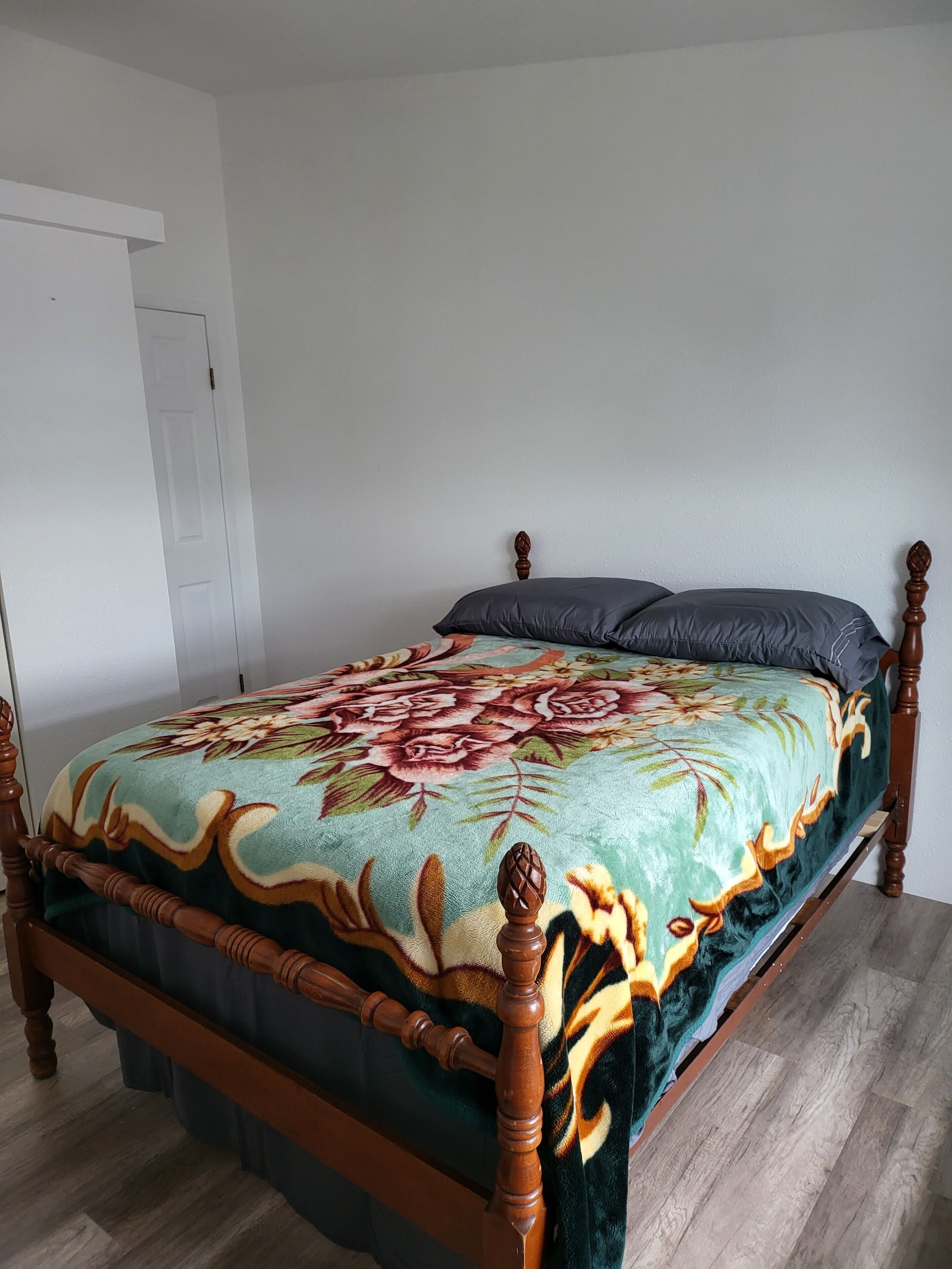 Una cama con una colcha estampada con flores, un cabecero de madera y una puerta blanca al fondo.