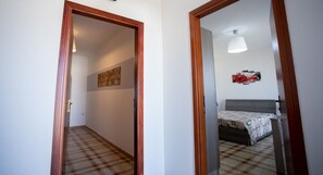 Un couloir menant à une chambre à coucher, où se trouvent un lit, un luminaire fixé au mur et un tableau.