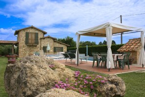 A stone house with a pool, outdoor seating, and a covered area.