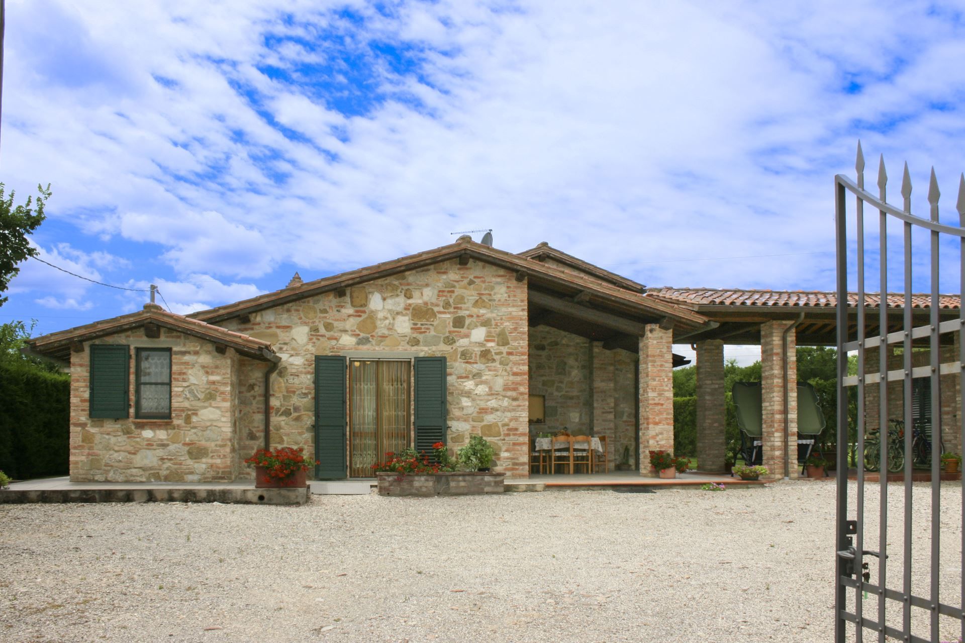A stone house with a gravel driveway and a covered patio area.