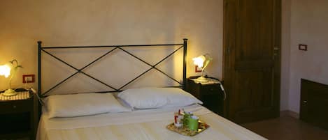 Ein ordentlich bezogenes Bett mit einer gestreiften Tagesdecke, zwei Nachttische mit Lampen, eine Holztür und ein kleines Tablett mit Tassen und einem Löffel auf dem Bett.