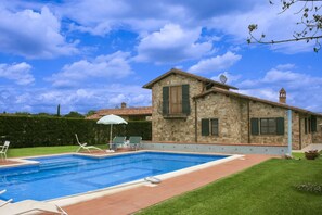 A stone house with a swimming pool, green shutters, and a satellite dish.