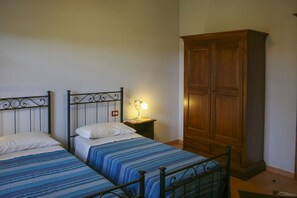Une chambre avec deux lits simples, une table de chevet avec une lampe et une armoire en bois.