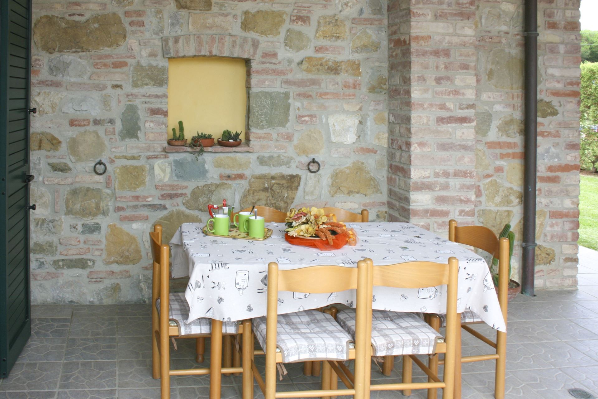 A stone wall with a window, a table with chairs, and a tray with food and drinks.
