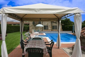 Un espace extérieur abrité avec une piscine, une table entourée de chaises et, au fond, un bâtiment en pierre.