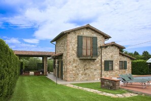 Une maison en pierre avec un patio, un espace couvert et une pelouse.