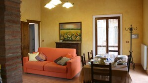 Ein Essbereich mit einem Tisch für zwei Personen, einer Couch mit Kissen, einem Gemälde von Sonnenblumen und einer Kristallleuchter.