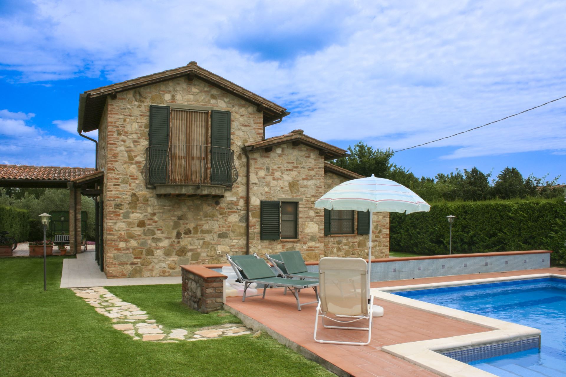Une maison en pierre avec une piscine, un espace salon extérieur et une pergola dotée d’un parasol.