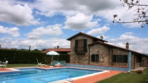Ein Steinhaus mit Swimmingpool, Rasen und Gartenmöbeln.