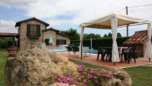 Ein Steinhaus mit Pool, Sitzgelegenheiten im Freien und einer überdachten Terrasse.