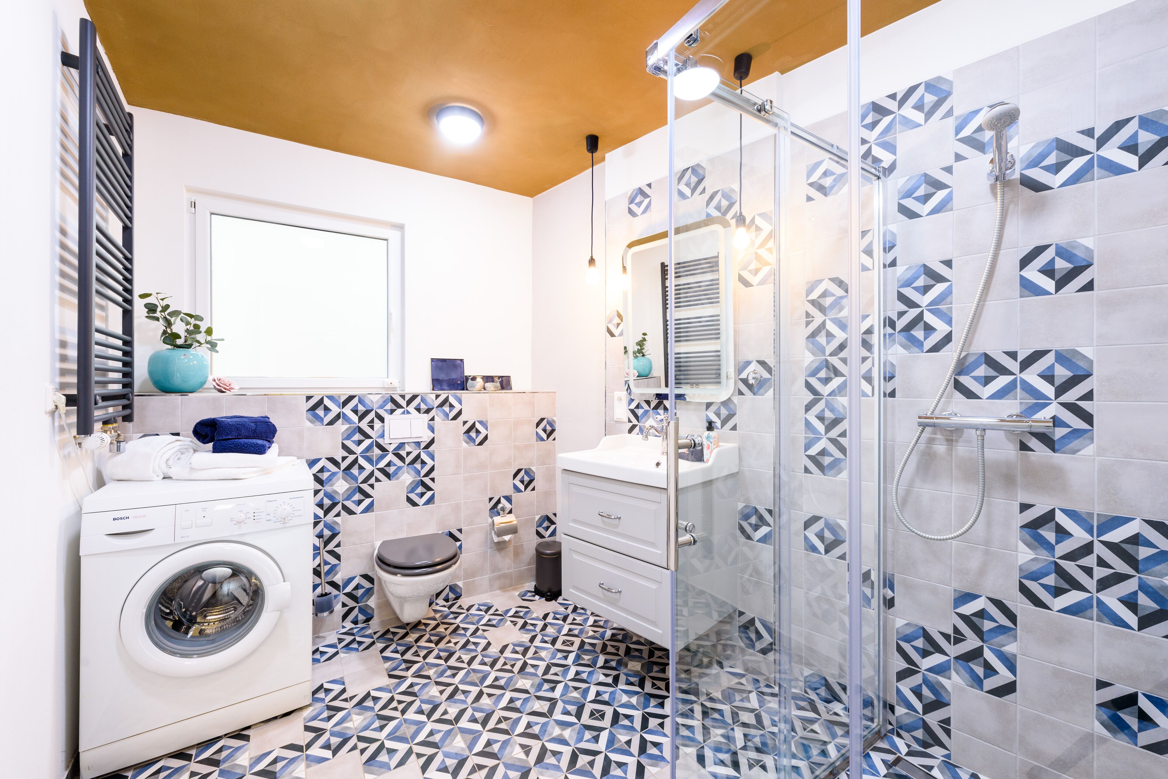 A modern bathroom with a washing machine, a toilet, a sink, and a shower enclosure.