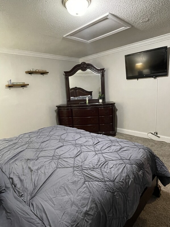 A bedroom with a bed, dresser, mirror, and TV.
