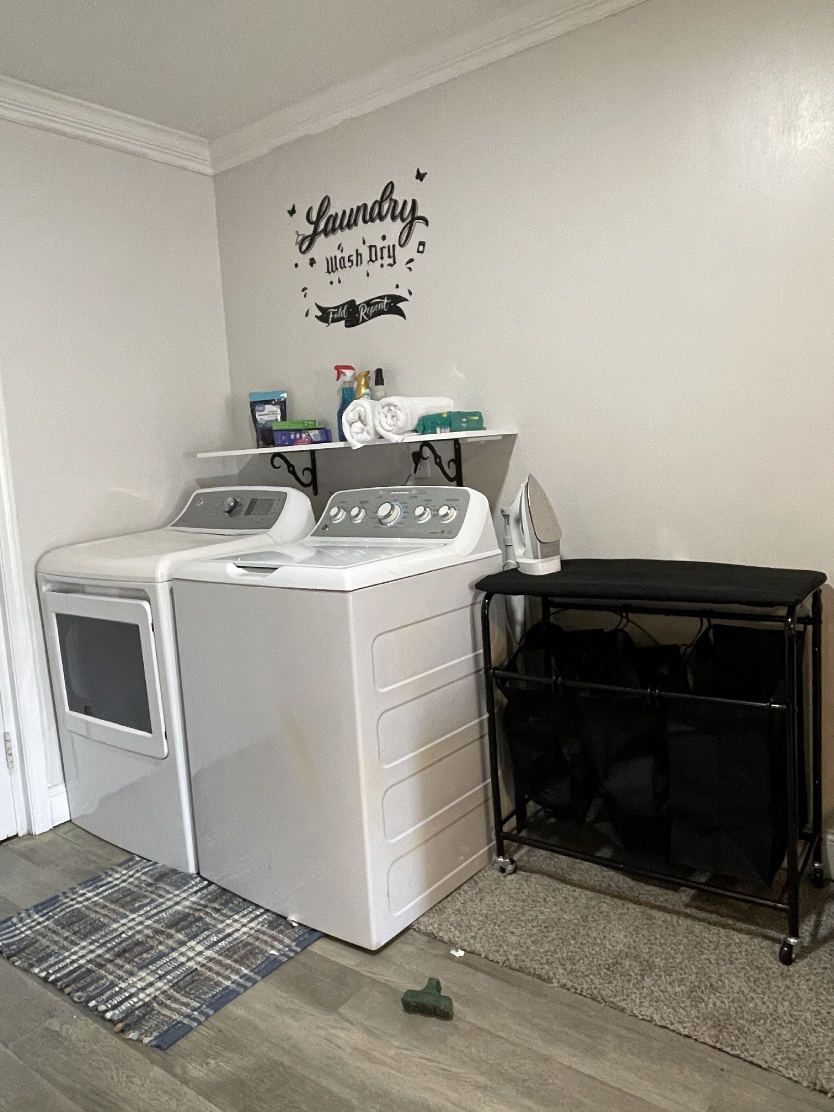 Un área de lavandería con lavadora, secadora y un estante en la pared con productos de limpieza.